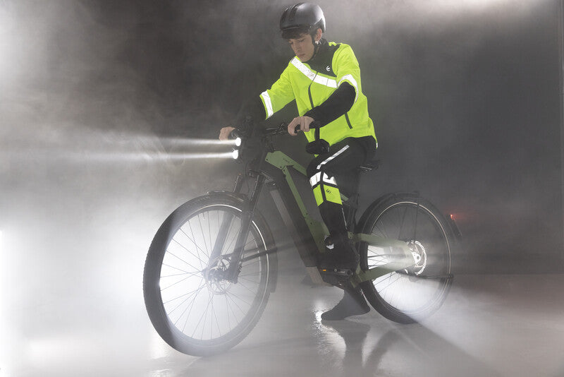 Cycliste éclairé et réfléchissant à vélo dans la pluie et le brouillard de nuit