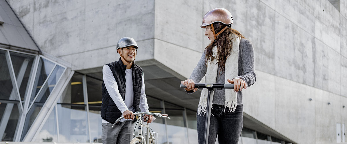 Cycliste et utilisatrice de trottinette électrique portant un casque en ville