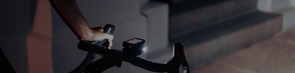 Lampe avant Ravemen allumée sous un compteur, sur le guidon d'un vélo de route en ville